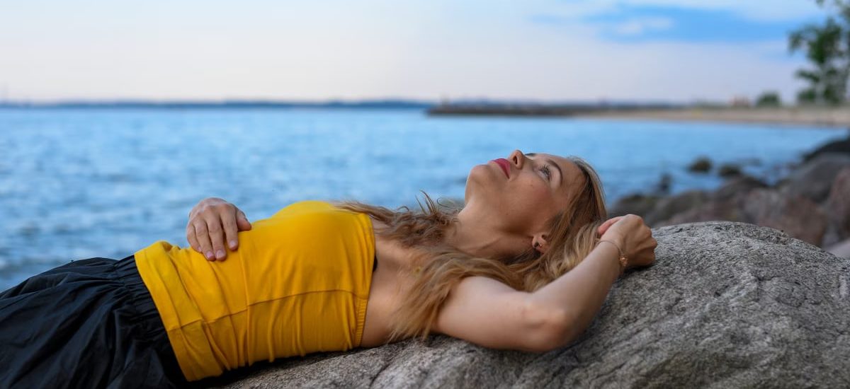 A woman peacefully relaxes on rocks by the sea in Tallinn during a calm summer day.