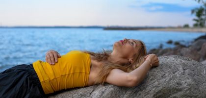 A woman peacefully relaxes on rocks by the sea in Tallinn during a calm summer day.