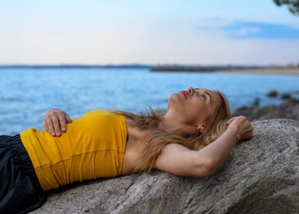 A woman peacefully relaxes on rocks by the sea in Tallinn during a calm summer day.