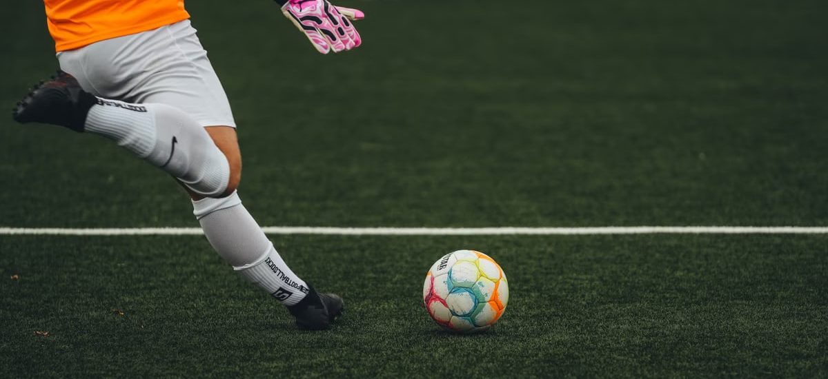 A soccer goalkeeper prepares to kick a colorful ball on a grass field.