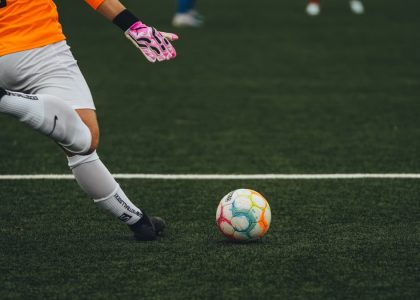 A soccer goalkeeper prepares to kick a colorful ball on a grass field.